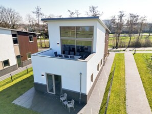 A modern building with a flat roof, large windows, and a patio area with chairs.