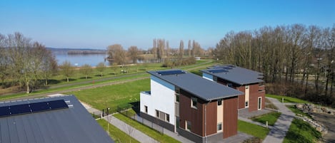 Un edificio moderno con paneles solares, un área con césped y un lago al fondo.
