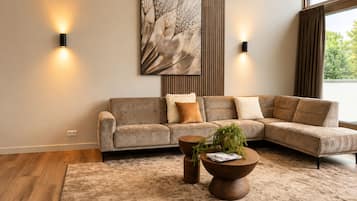 Een moderne woonkamer met een modulaire bank, twee wandlampen, een groot abstract schilderij en een houten vloer.
