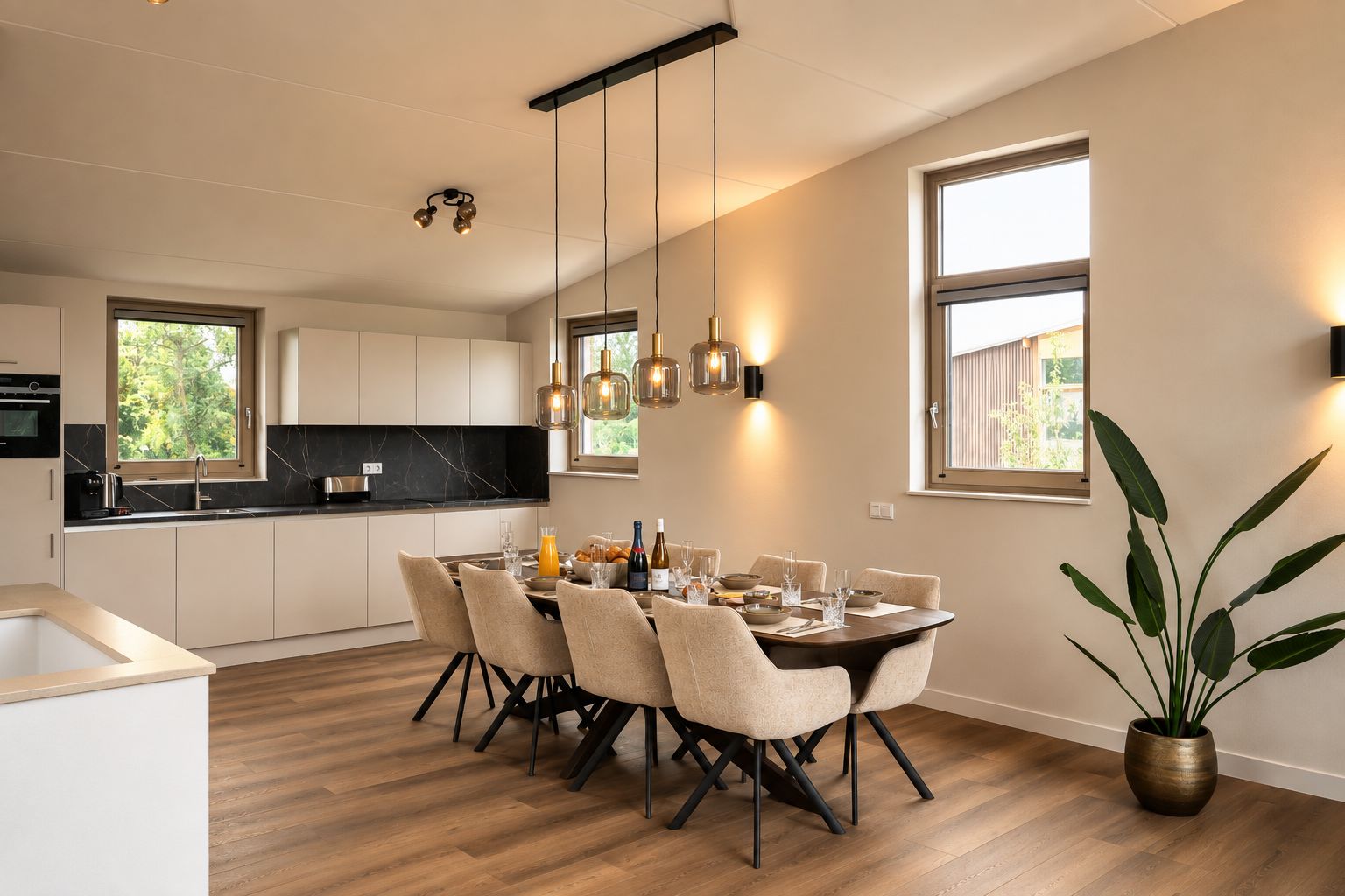 A modern kitchen with a dining area, featuring a wooden table set for six, a large window, and a potted plant.