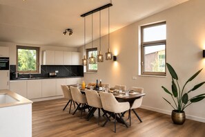 Eine moderne Küche mit Essbereich, ausgestattet mit einem Holztisch für sechs Personen, einem großen Fenster und einem Blumentopf.