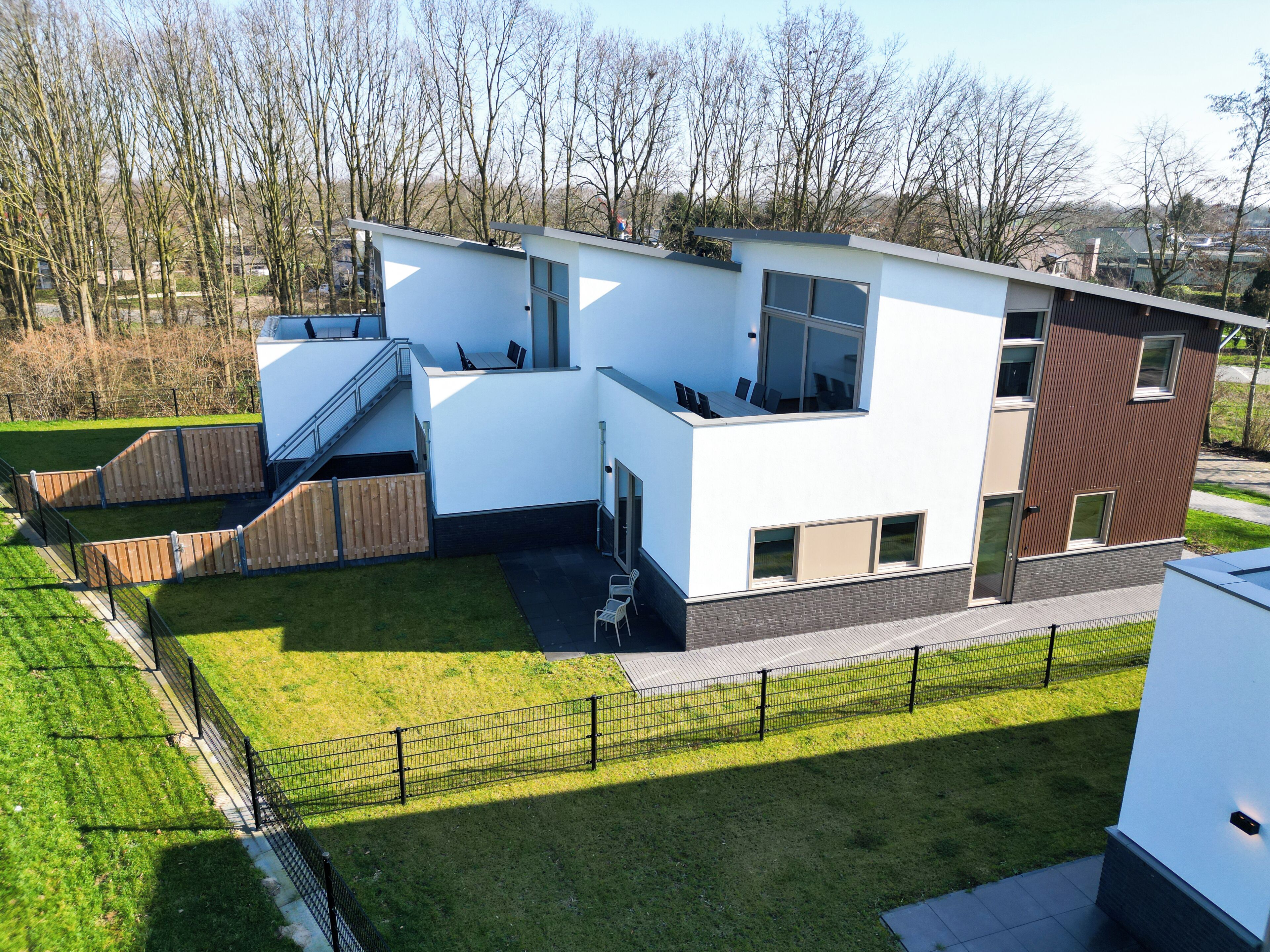 Une maison moderne à deux étages, dotée d’un toit plat, de grandes fenêtres et d’un petit espace extérieur aménagé pour s’asseoir.