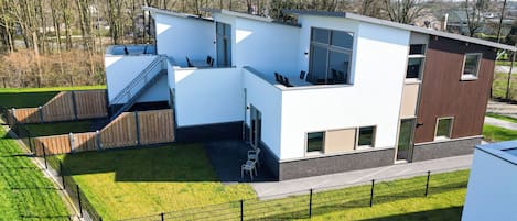 Una casa moderna de dos pisos con techo plano, ventanas amplias y un pequeño espacio al aire libre para sentarse.