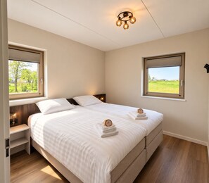 Una camera d'albergo con un letto grande, due comodini, una lampada da comodino, un lampadario e due finestre con vista sul verde.