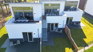 A modern two-story house with a flat roof, large windows, and a covered outdoor seating area. - Experience the ultimate holiday feeling in a stylish waterfront holiday home, with the beach within walking distance.<br>Located close to the Hoge Veluwe National Park and the beautiful Posbank – ideal for nature lovers, hikers, and cyclists. (Giesbeek)