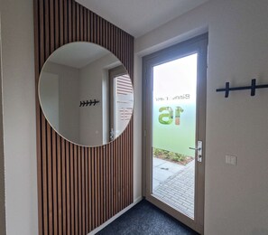 Un couloir avec un mur lambrissé en bois, un miroir rond et une porte dotée d’un panneau en verre dépoli.