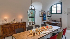 Un comedor con una larga mesa de madera, sillas, candelabros e lámparas colgantes.
