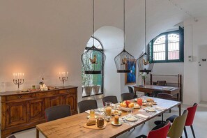 Un comedor con una larga mesa de madera, sillas, candelabros e lámparas colgantes.