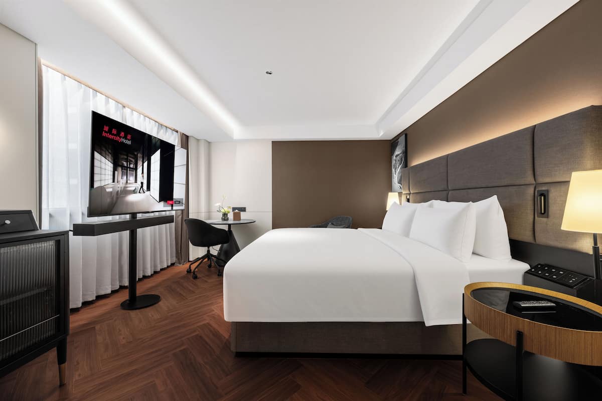 Ein Hotelzimmer mit Bett, Schreibtisch, Stuhl, Lampe und Fernseher.