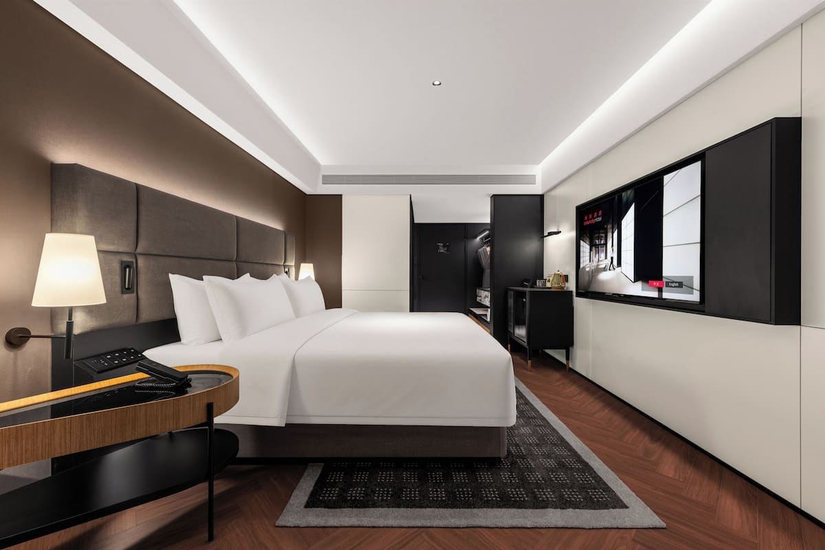 Ein modernes Hotelzimmer mit einem großen Bett, einem Schreibtisch, einem Spiegel und einem Kleiderschrank.
