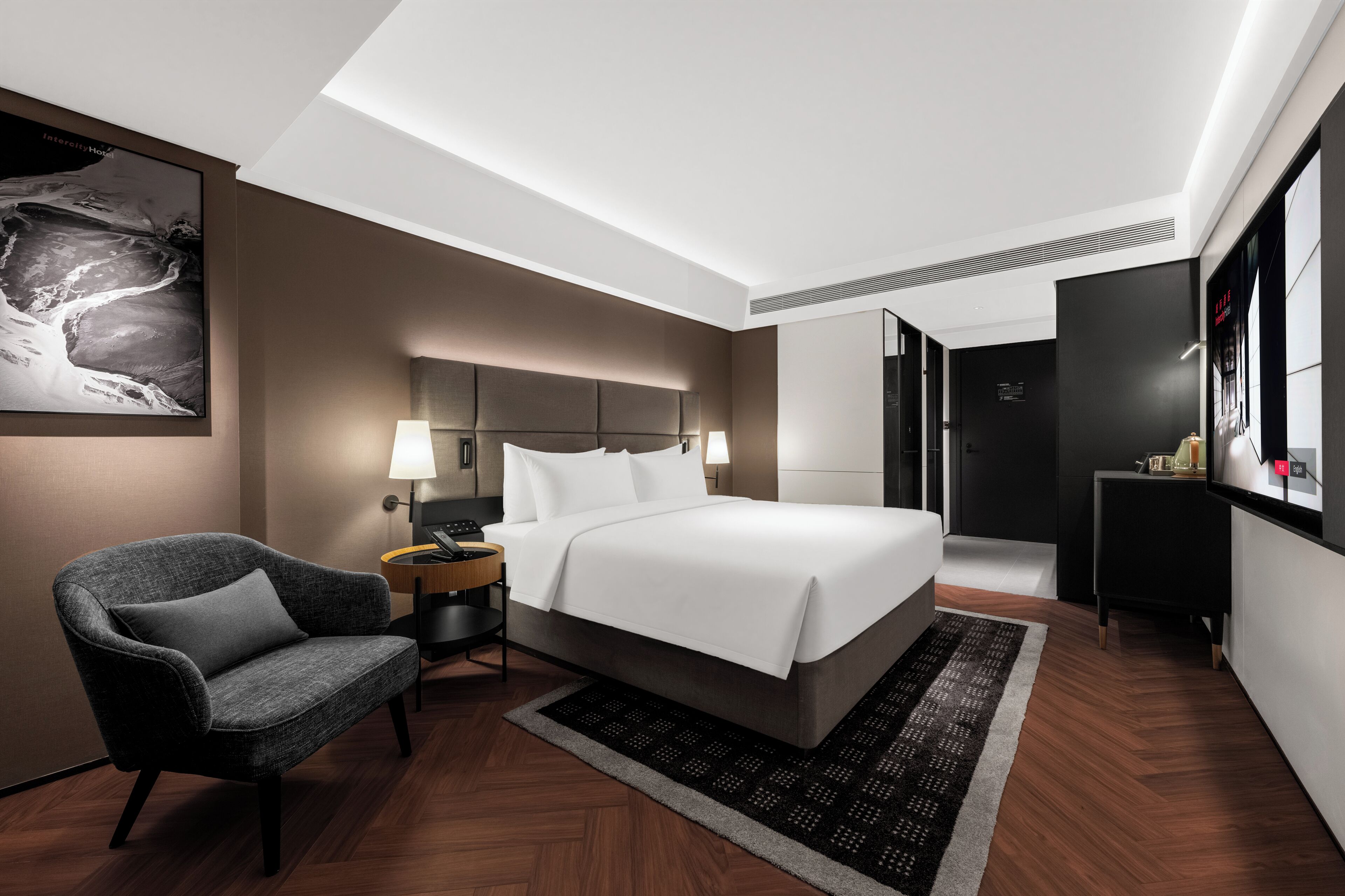 A modern hotel room with a large bed, a chair, a nightstand, and a wall-mounted TV.