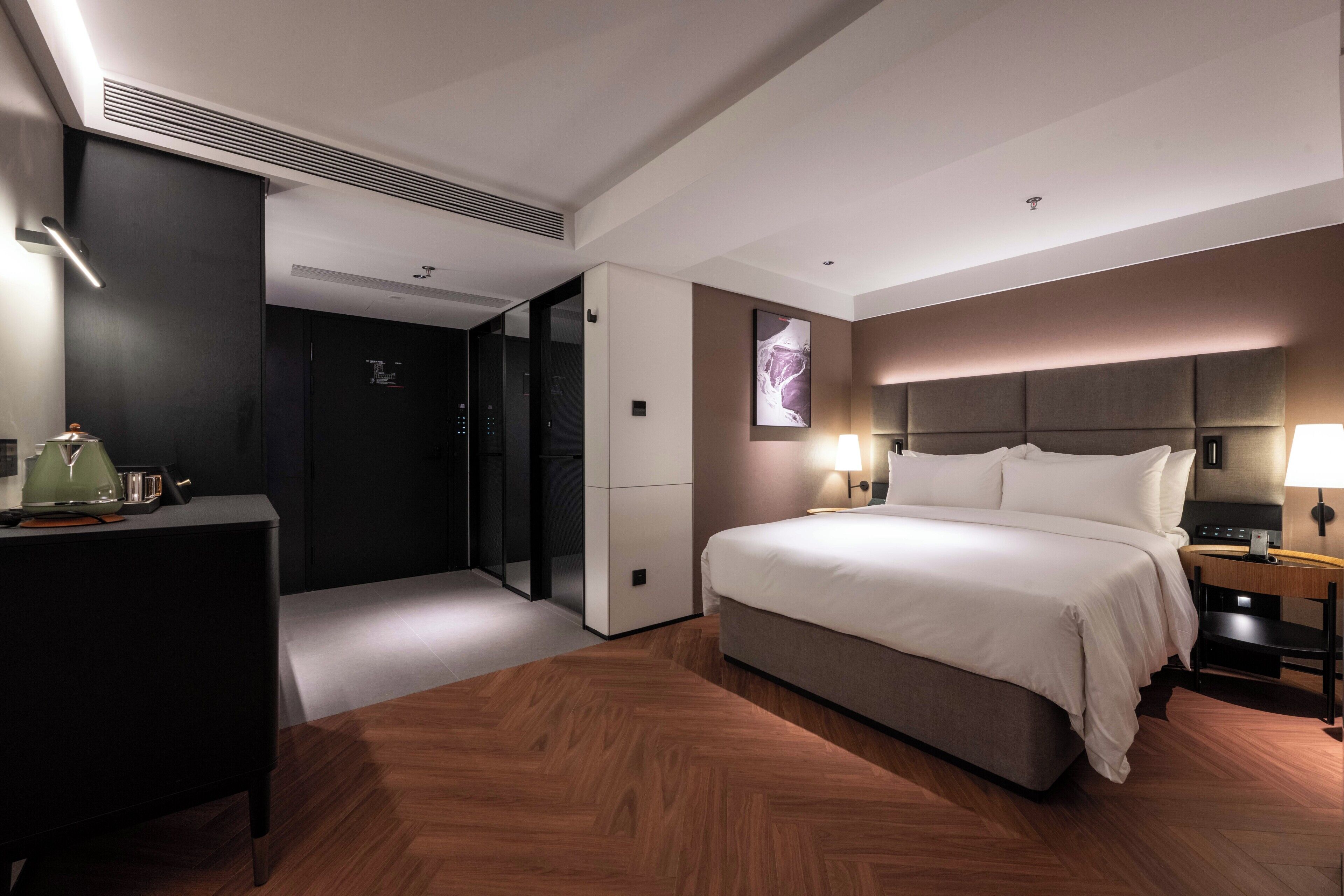 Habitación de hotel moderna con una cama grande, mesita de noche, lámpara y vistas a la ciudad a través de un ventanal.