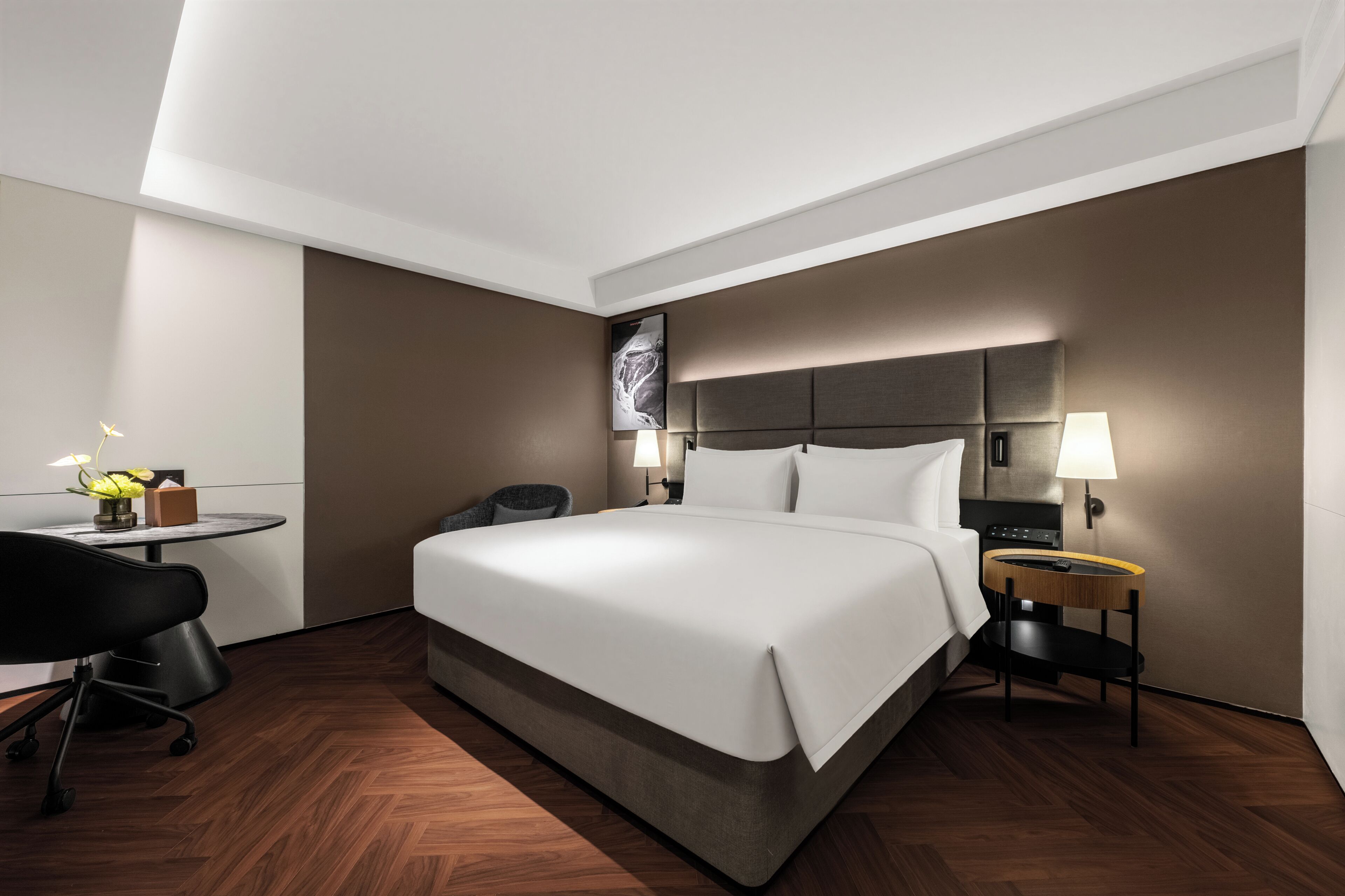 A modern hotel room with a large bed, bedside tables, a desk, and a chair.