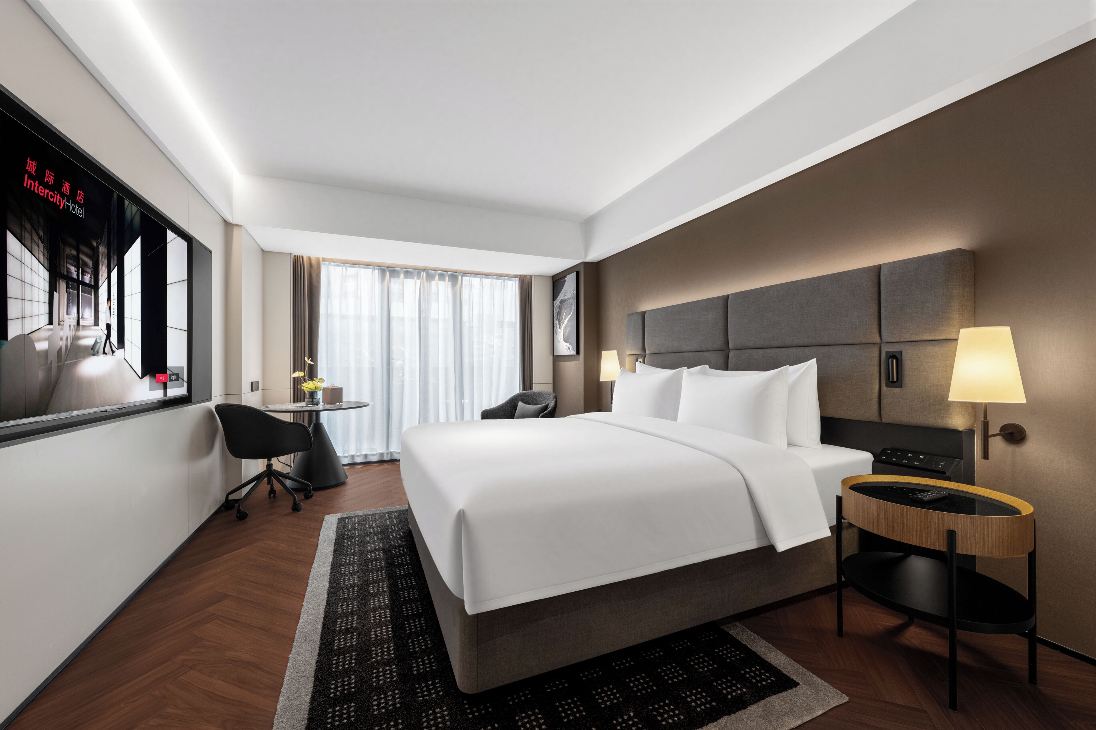 Ein modernes Hotelzimmer mit einem großen Bett, einem Schreibtisch, einem Sessel und Blick auf die Stadt.