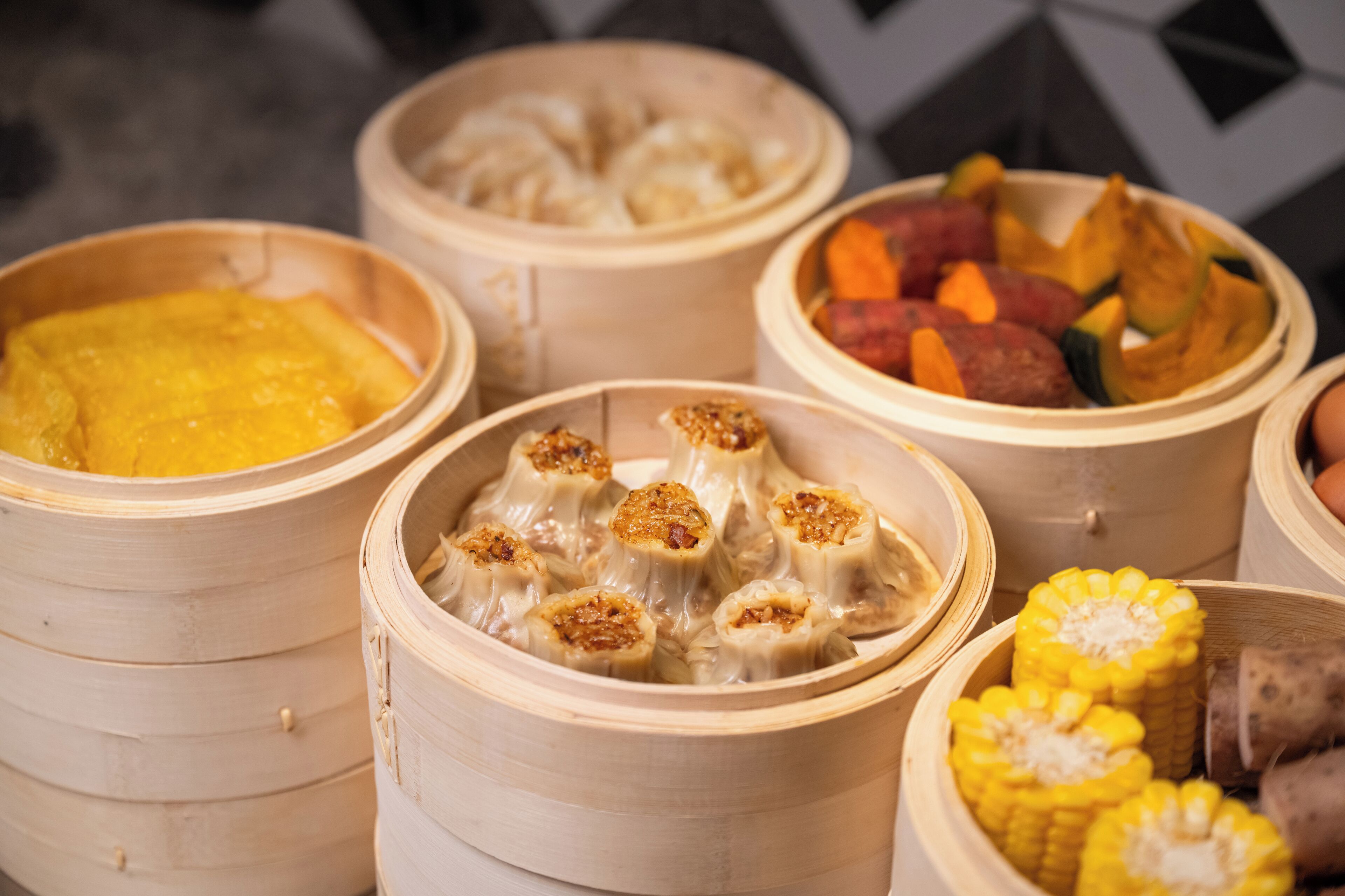 A variety of food items in bamboo steamers, including dumplings and corn.