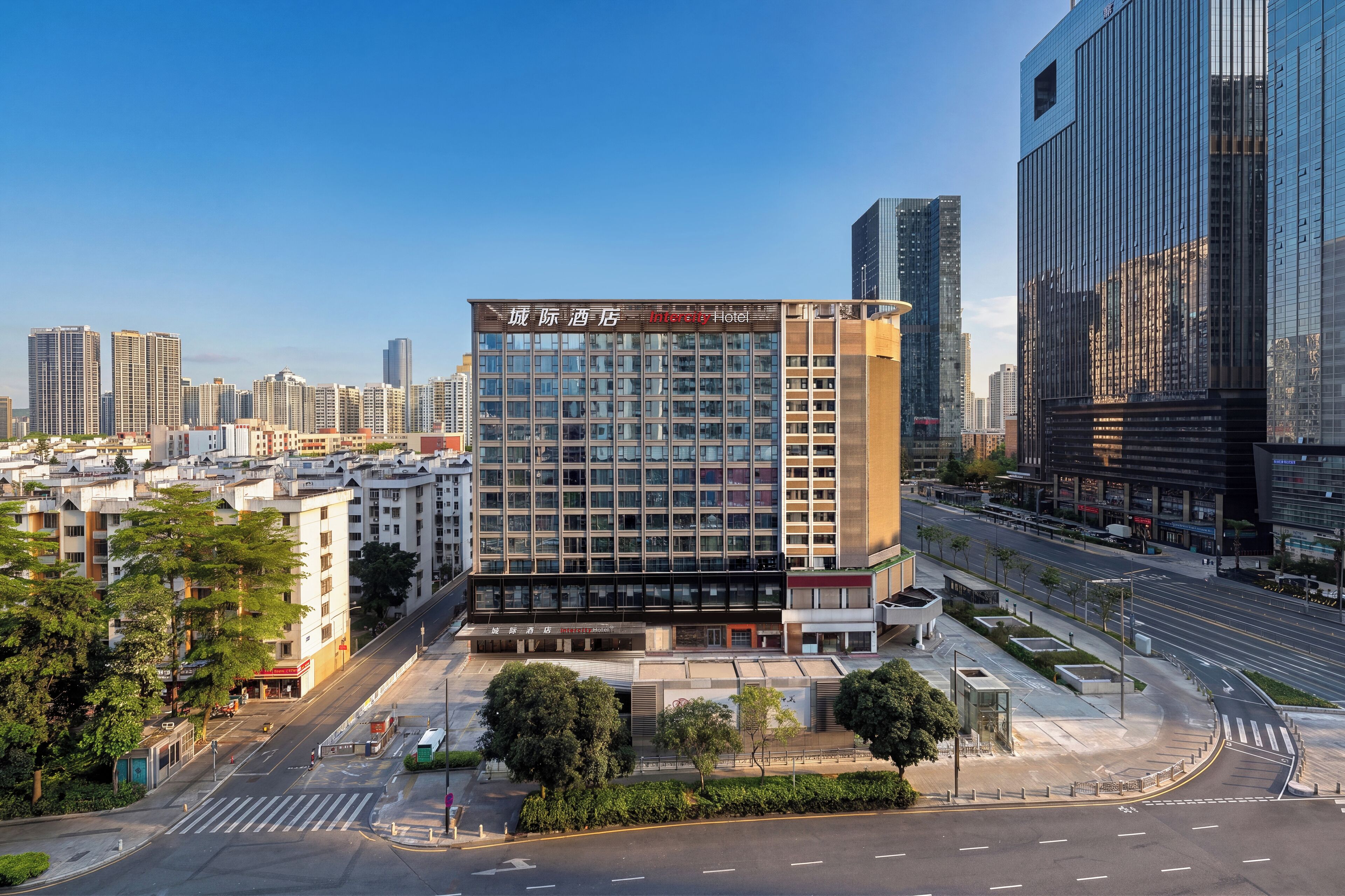 A modern hotel with a glass facade, located in an urban setting with high-rise buildings in the background.