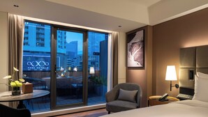 A hotel room with a large window, a bed, a chair, a small table with a lamp, and a wall-mounted phone. - Intercity Hotel Futian Convention (Shenzhen)