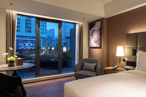 A hotel room with a large window, a bed, a chair, a small table with a lamp, and a wall-mounted phone. - Intercity Hotel Futian Convention (Shenzhen)
