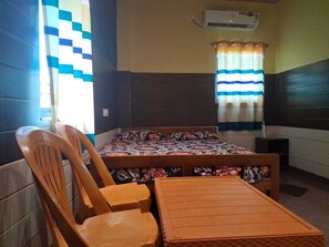 A room with a bed, two wooden chairs, a small table, an air conditioning unit, and a window with a striped curtain. - Hotel Aditya Palace (Maharajgang)