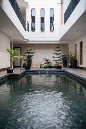 Une piscine intérieure moderne, agrémentée de plantes en pot, dotée d’un sol carrelé et d’un plafond haut avec de grandes fenêtres.