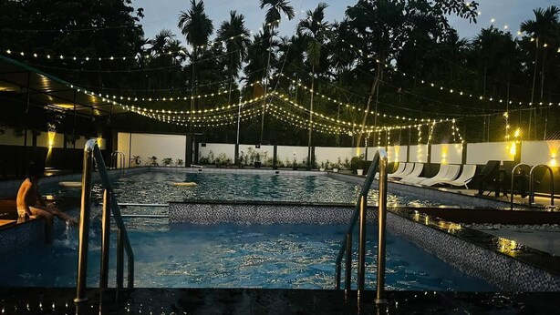 En swimmingpool med fliseterrasse, omgivet af palmer og lyskæder.