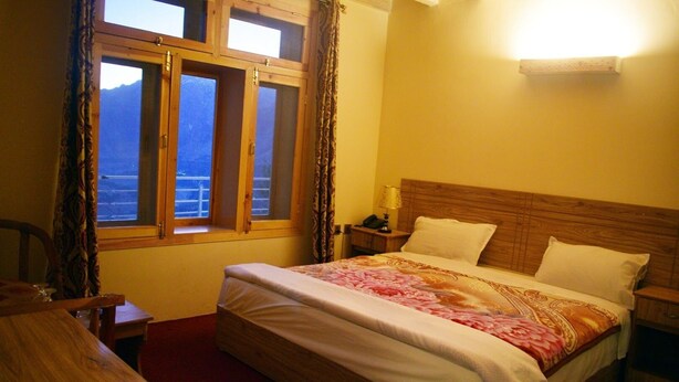 Un dormitorio con cama de madera, mesita de noche, lámpara, ventana con cortinas y vista al exterior.