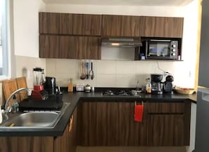 A kitchen with wooden cabinets, a microwave, a stove, and a sink. - Mareva Dreams · A safe and welcoming place (San Clemente de Lima)