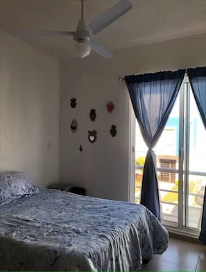 A bedroom with a bed, ceiling fan, window with curtains, and wall decorations. - Mareva Dreams · A safe and welcoming place (San Clemente de Lima)