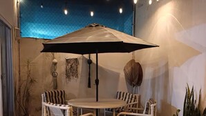 A patio with a round table and four chairs, an umbrella, string lights, and decorative wall hangings. - Mareva Dreams · A safe and welcoming place (San Clemente de Lima)