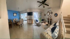 A living room with a sofa, a dining table with chairs, a TV, and a ceiling fan. - Mareva Dreams · A safe and welcoming place (San Clemente de Lima)