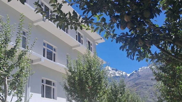 Un immeuble à plusieurs étages, doté d’une façade blanche, entouré d’arbres et adossé à un paysage montagneux.