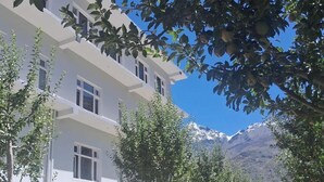 Un immeuble à plusieurs étages, doté de fondations en pierre, entouré d’arbres et adossé à un paysage montagneux.