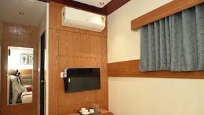 A hotel room with a wooden panel wall, a mounted TV, a small table with cups and glasses, and a window with curtains.