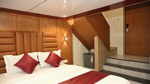 A bedroom with a bed, a nightstand, a small refrigerator, and a staircase leading to an upper level.