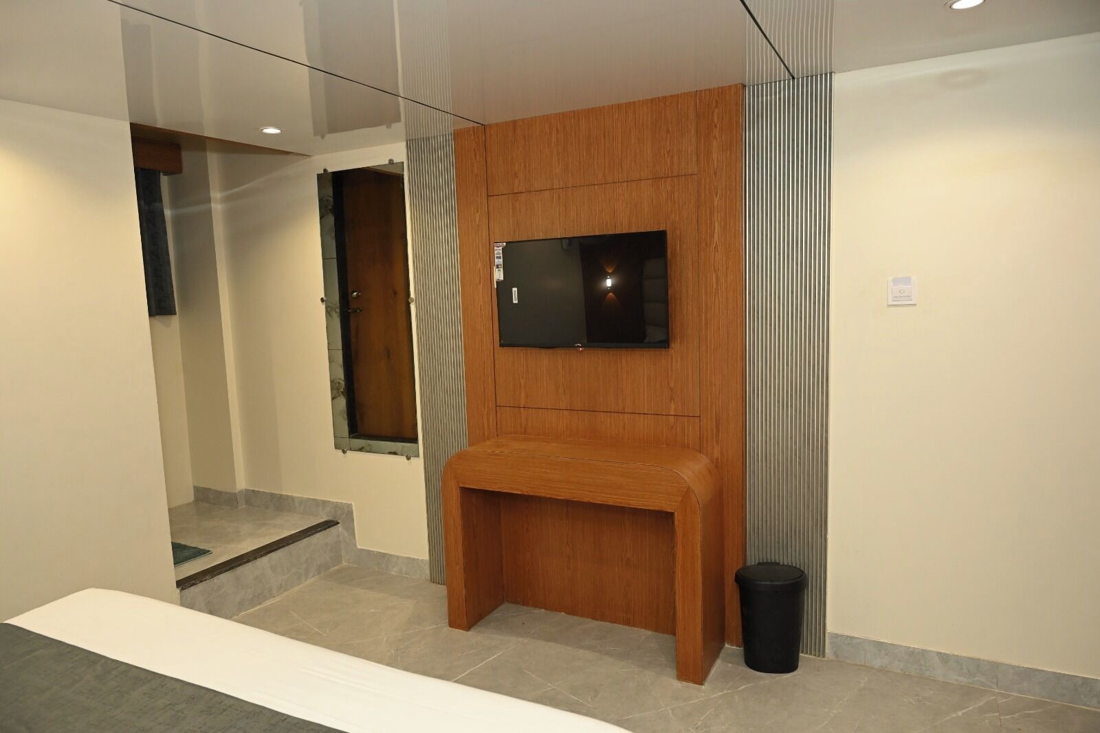 Ein modernes Hotelzimmer mit einer Holzbank, einem an der Wand befestigten Fernseher und einem Mülleimer.