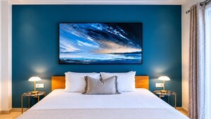A hotel room with a large bed, two bedside lamps, a nightstand, and a painting of a cloudy sky. - Relaxing Garden Apartment with Sea Views in Finca Cortesin Resort (Casares)