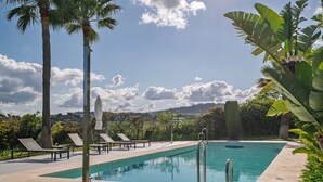 A swimming pool with lounge chairs, palm trees, and a clear sky. - Relaxing Garden Apartment with Sea Views in Finca Cortesin Resort (Casares)
