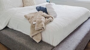 A modern bedroom with a large bed, a grey bench, and two windows with a view. - Brown Family Vacation Home - 4 Bedrooms- 3 baths (Leduc)