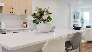 A modern kitchen with a white countertop, a decorative vase with flowers, and a bar area with chairs. - Brown Family Vacation Home - 4 Bedrooms- 3 baths (Leduc)