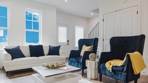 A modern living room with a white sofa, two dark armchairs, a coffee table, and a staircase in the background. - Brown Family Vacation Home - 4 Bedrooms- 3 baths (Leduc)