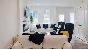 A living room with a white sofa, a blue armchair, a TV, and a window with a view. - Brown Family Vacation Home - 4 Bedrooms- 3 baths (Leduc)