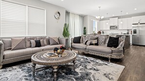 A modern living room with a sectional sofa, a round coffee table, and a kitchen area in the background. - A comfortable 3-bedroom home offers 5 beds and can accommodate up to 8 guests. (Rogers)