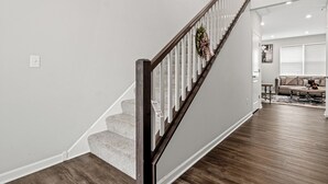 A staircase with a wooden handrail, carpeted steps, and a wall-mounted light switch. - A comfortable 3-bedroom home offers 5 beds and can accommodate up to 8 guests. (Rogers)
