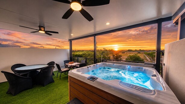 Een balkon met een jacuzzi, buitenmeubels en uitzicht op de zonsondergang.