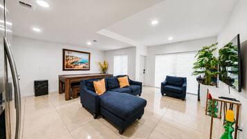 Amplia sala de estar con un conjunto de sofás, una mesa de comedor y un televisor montado en la pared.