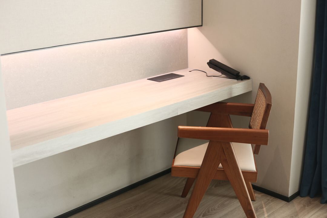 Un escritorio en esquina con una silla, un teléfono y un objeto pequeño sobre la superficie.