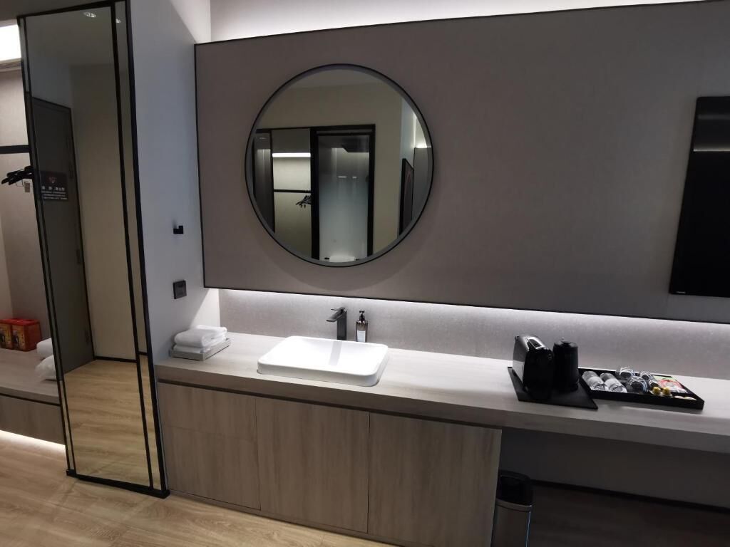 A modern bathroom with a large mirror, a white sink, and a towel rack.