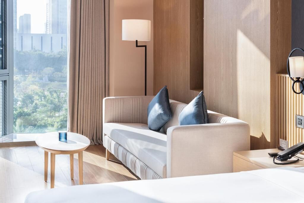 A modern hotel room with a sofa, a small round table, a lamp, and a phone on a bedside table.