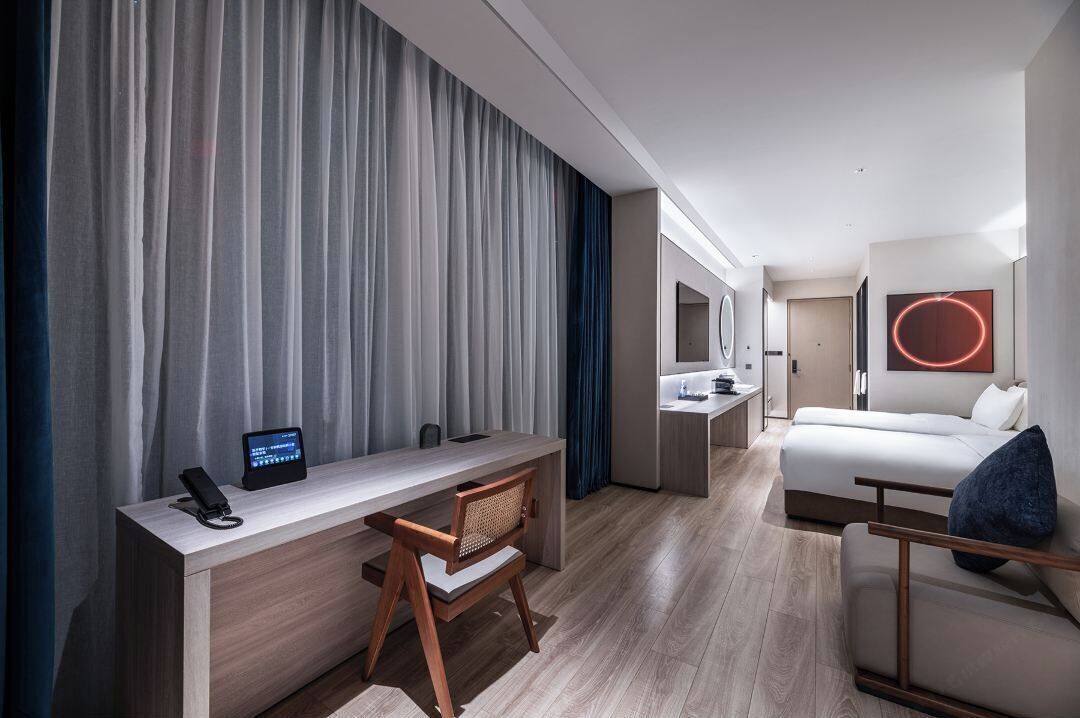 A modern hotel room with a desk, chair, bed, and a large mirror.
