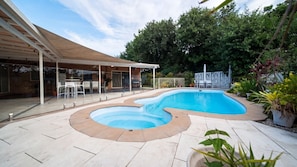 Une piscine au design incurvé, entourée d’un patio couvert aménagé avec des sièges.